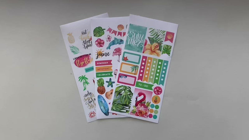 Female hands pick up and show in detail 3 sheets of stickers featuring a tropical June theme.