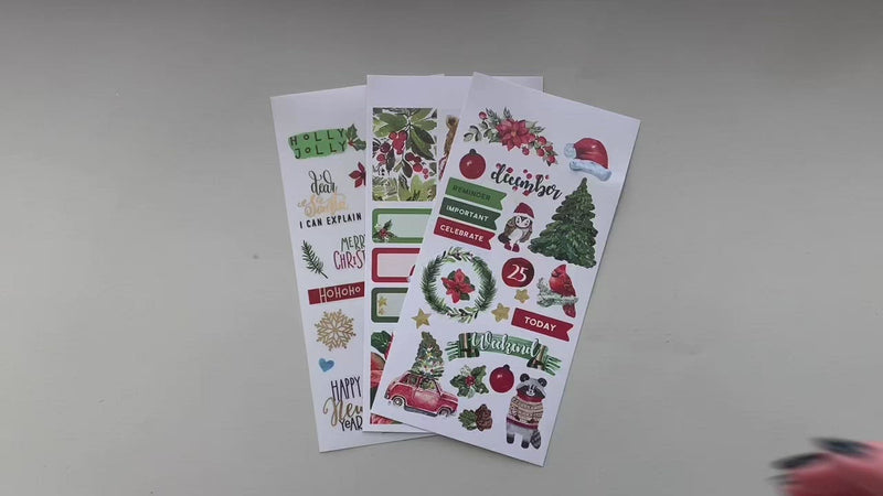 Female hands pick up and show in detail 3 sheets of planner stickers featuring Christmas.