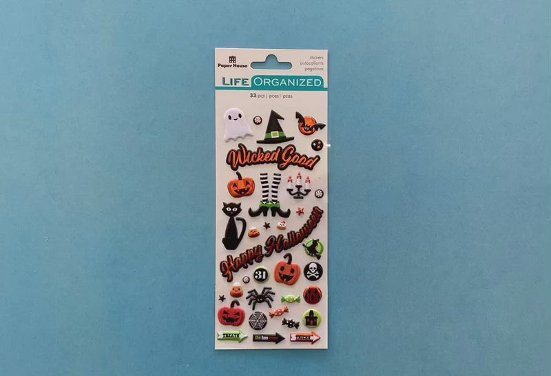 female hands displaying puffy stickers featuring illustrated pumpkins, ghosts, spiders and bats, on blue background with package.