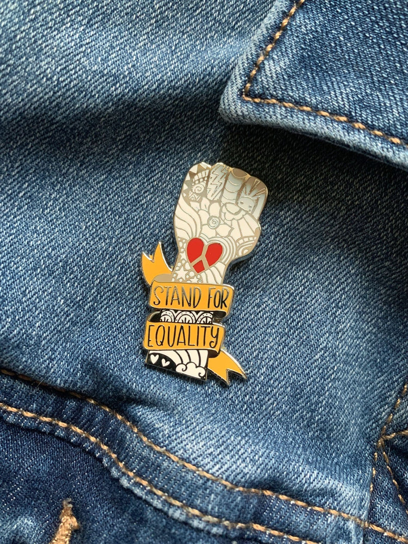 Stand for Equality enamel pin shown being used as a lapel pin for a denim jacket.