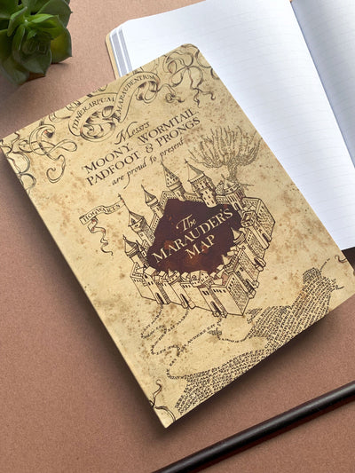 Harry Potter Marauder's Map softcover journal notebook shown laying on a desk. Journal cover features a Hogwarts castle illustration on beige background.
