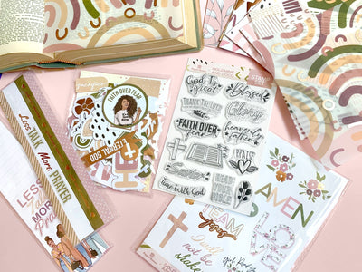 bible journaling craft kit items featuring papers, stickers and stamps are shown displayed on pink background.