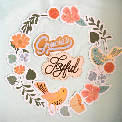 Craft kit featuring illustrated die cuts of birds, florals and words, arranged in a wreath pattern on white background.