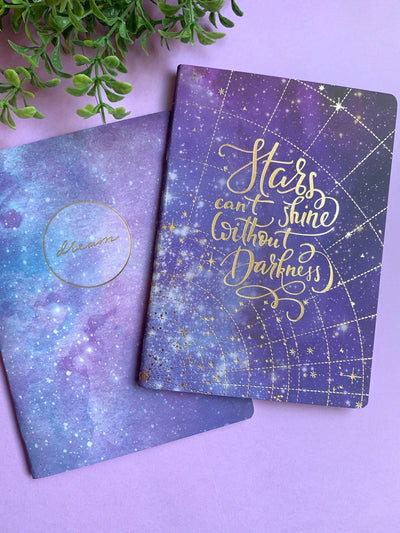 notebook set featuring blue and purple celestial theme with gold details are shown on purple background with a green plant.