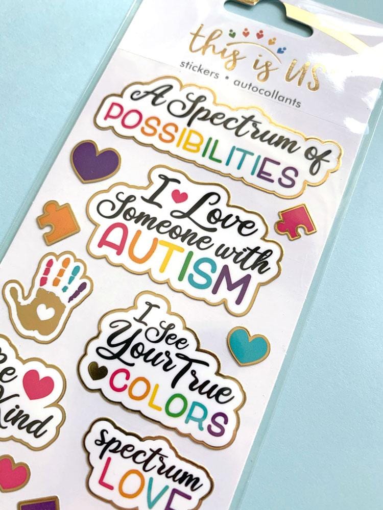 close up of foil stickers featuring an Autism theme with colorful, illustrated handprints, puzzle pieces and words of encouragement, shown in package on light blue background.