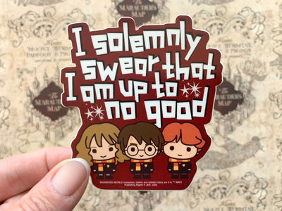 close up of Shaped Harry Potter laptop sticker shown in hand, featuring 3 chibi characters and "I solemnly swear…" sentiment, shown above a beige marauder's map pattern.