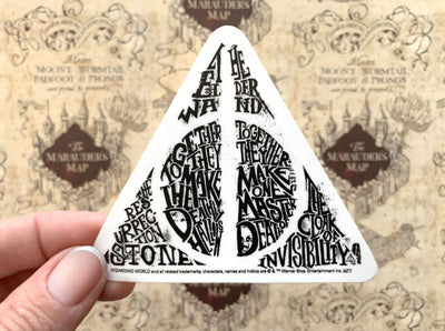 close up of vinyl laptop sticker featuring Harry Potter Deathly Hallows design shown black on white, held in hand over a marauder's map background.
