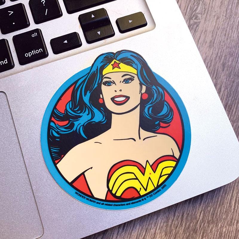 Shaped laptop sticker featuring the Wonder Woman portrait in illustrative style with blue, red and yellow details, shown on a silver laptop computer.