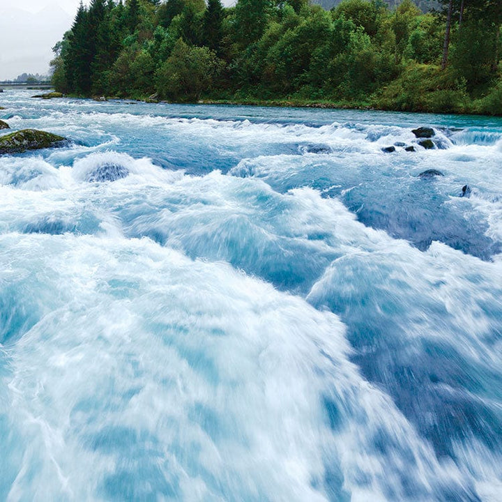 scrapbook paper featuring a photographic image of a rushing stream with greenery and mountains in the distance.