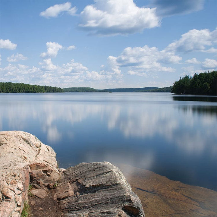 scrapbook paper featuring a photographic image of a lake reflecting the clouds with a rocky shore in the foreground.