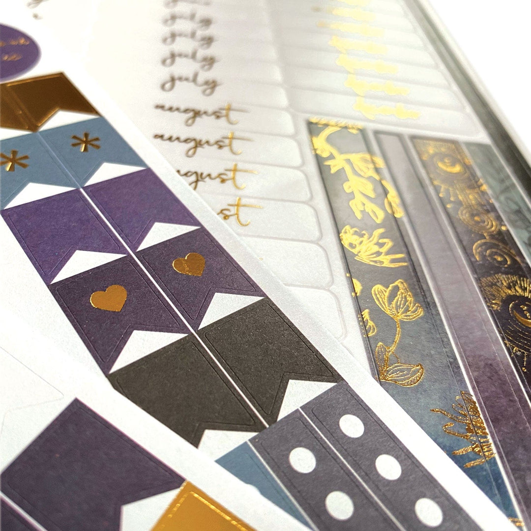 PL-2016E - Weekly Planner - Undated Celestial - Spiral-bound planner pages displaying purple, blue, and gold decorative washi tape strips and month tabs with celestial-inspired designs