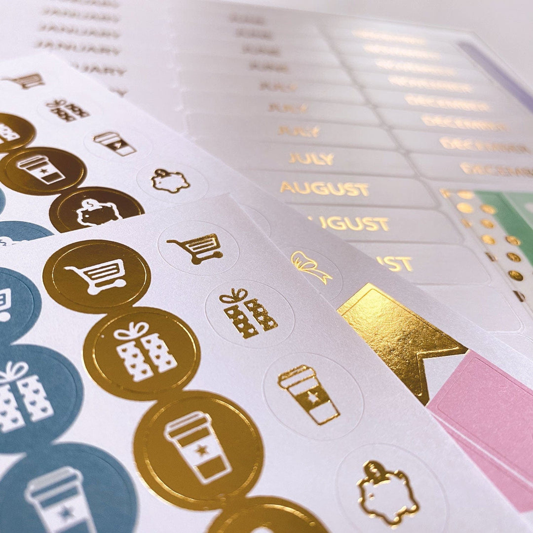 PL-2023E - Weekly Planner - Boho Rainbow - Gold foil stickers and calendar pages with month labels and decorative icons in blue, gold, and pink tones