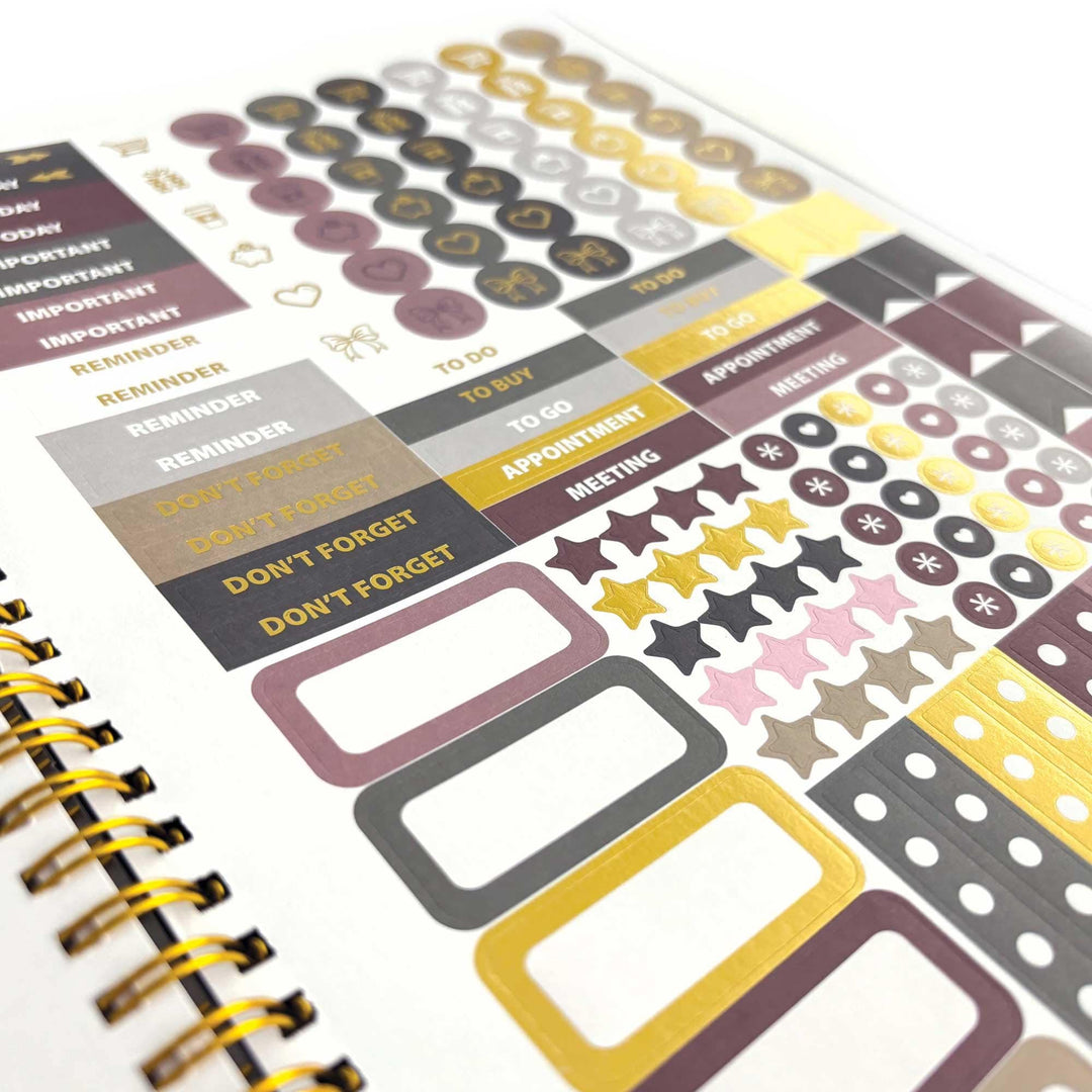 PL-2036E - Books &amp; Flowers 12 Month Undated Planner - Spiral-bound planner page with burgundy, gold, and gray stickers including circles, stars, text labels, and checkbox elements