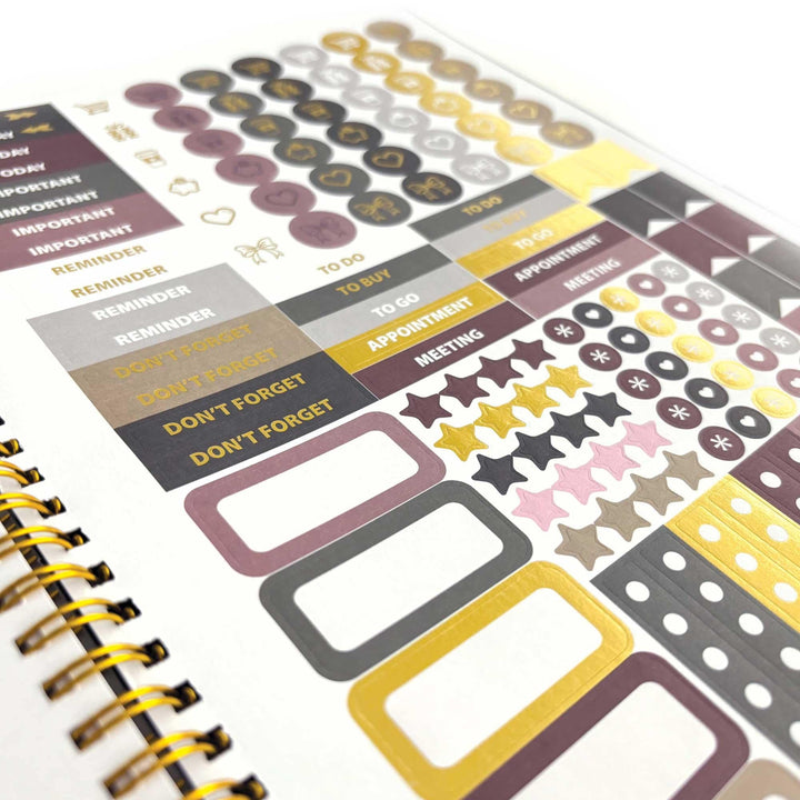 PL-2036E - Books &amp; Flowers 12 Month Undated Planner - Spiral-bound planner page with burgundy, gold, and gray stickers including circles, stars, text labels, and checkbox elements