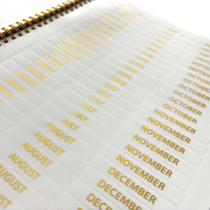 PL-2040E - Through the Keyhole 12 Month Undated Planner - Spiral-bound planner with white pages showing gold-foil month tabs arranged vertically from January through December