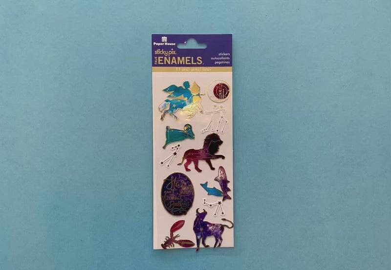 female hands display foil stickers featuring celestial illustrations in purples and blues with faux enamel gold accents, on blue background with package.