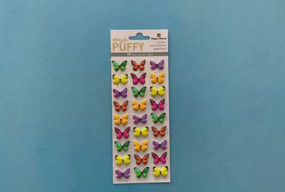 female hands displaying puffy stickers featuring colorful, photo real butterflies, shown on blue background with package.