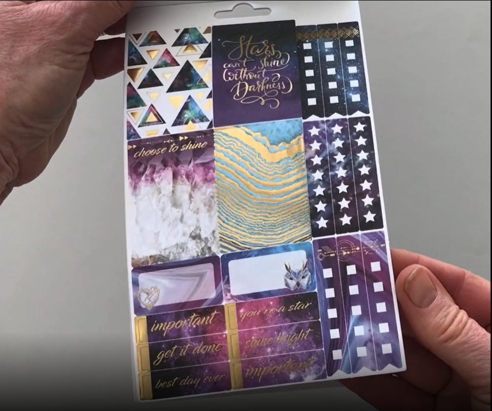 Female hands pick up and flip through the pages of the "Stargazer" planner stickers booklet to show each page of stickers in detail. There are four pages in this sticker book by Paper House Productions.