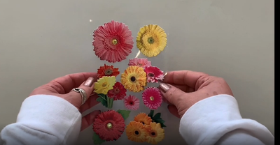 Female hands pick up and show front and back of photo real 3D decorative stickers featuring colorful gerbera daisies.