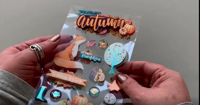 Female hands pick up and show front and back of 3D scrapbook stickers featuring watercolor foxes, leaves and pumpkins.