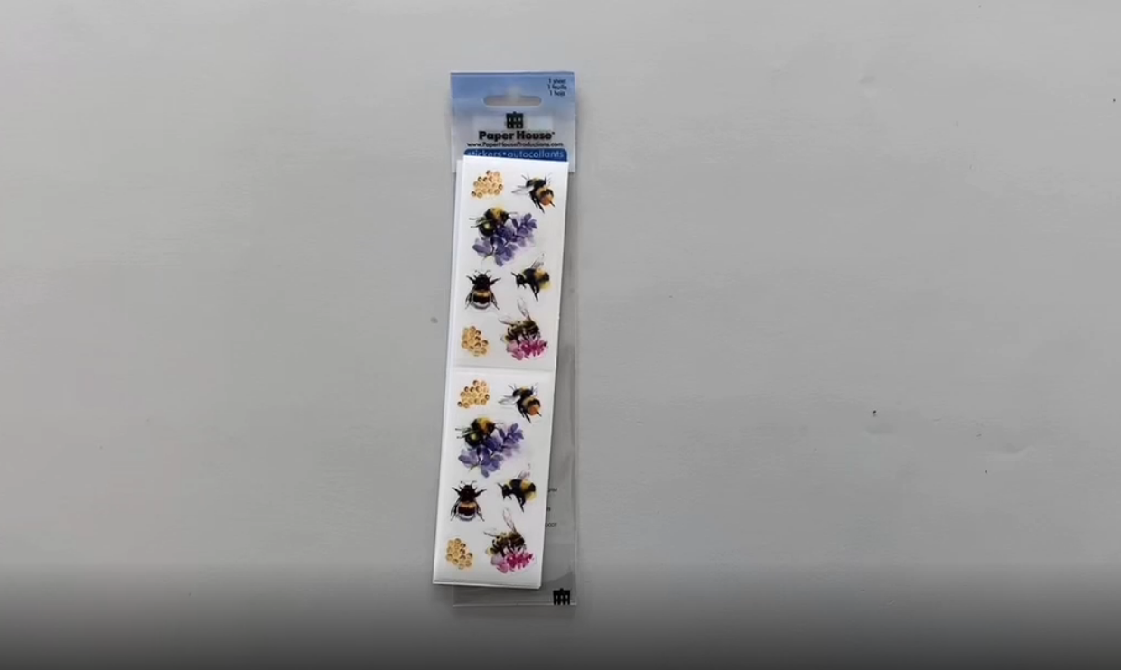 Female hands pick up and unfold a sheet of decorative stickers featuring watercolor bees and places them back on the table.