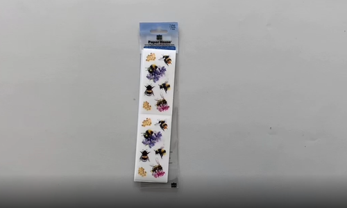 Female hands pick up and unfold a sheet of decorative stickers featuring watercolor bees and places them back on the table.