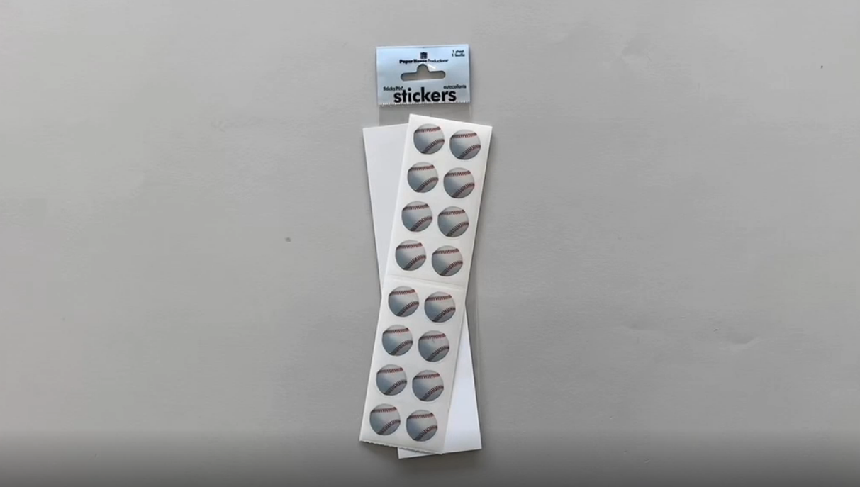 Female hands pick up a sheet of stickers featuring photo real baseballs. 
