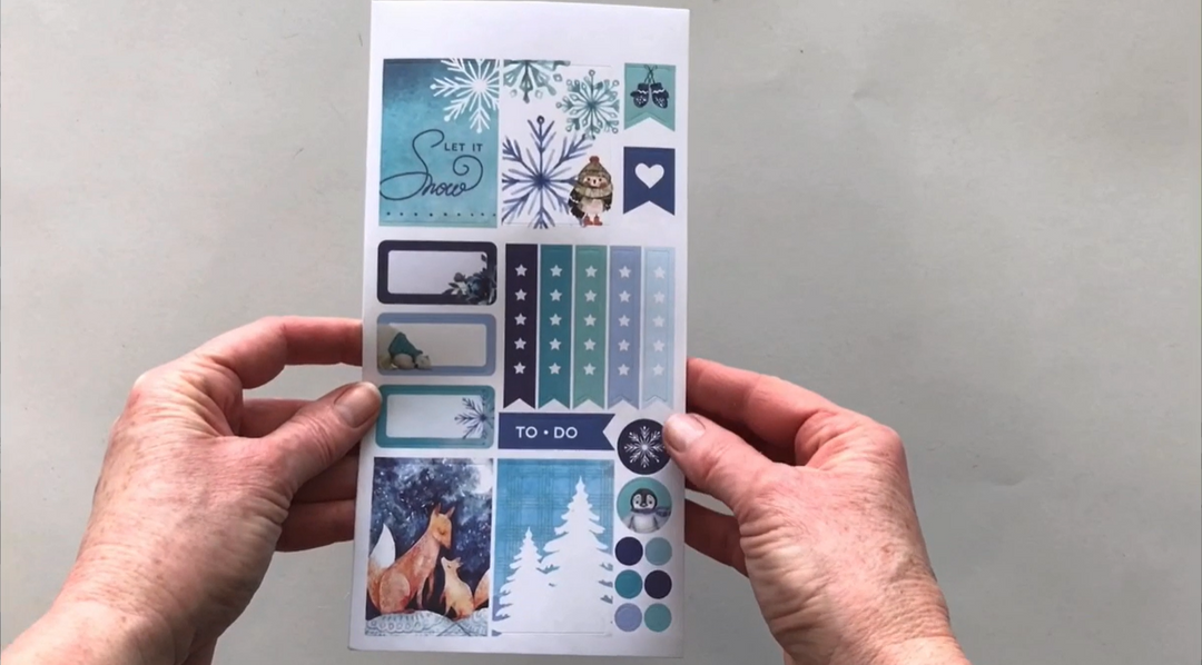Female hands pick up 3 sheets of stickers in this January-Winter kit to show each page of stickers in detail. 
