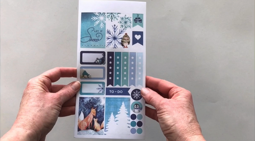 Female hands pick up 3 sheets of stickers in this January-Winter kit to show each page of stickers in detail. 