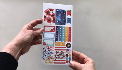 Female hands pick up and show in detail 3 sheets of planner stickers featuring a patriotic summer theme.