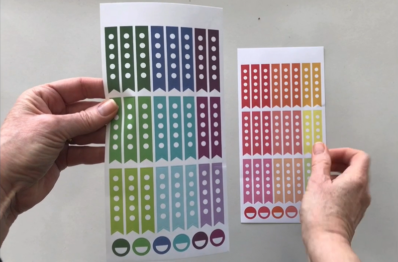Female hands pick up and show in detail 2 sheets of colorful checkbox planner stickers.