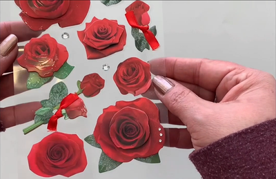 Female hands pick up 3D scrapbook stickers featuring photo-real red roses.