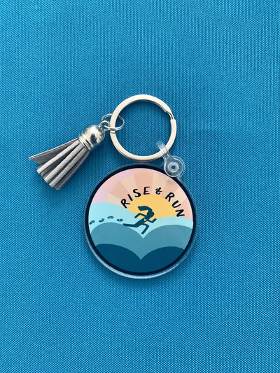 cute keychain featuring an illustration of a running person with blue and silver details and tassel, shown on blue background.