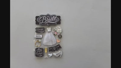 Female hands pick up and show 3D scrapbook stickers featuring a wedding dress, champagne and black and white chalk signs.