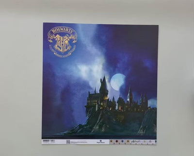 female hands display Harry Potter scrapbook paper featuring Hogwarts at night on one side and a colorful pattern on the reverse.