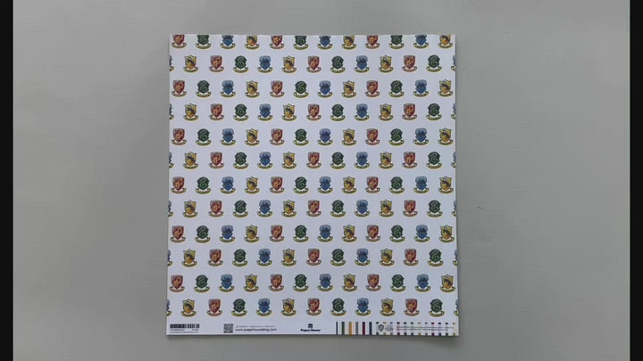 Female hands pick up harry potter scrapbook paper featuring a pattern of the multi-colored House Crests on one side and a pattern of colored stripes on the reverse.