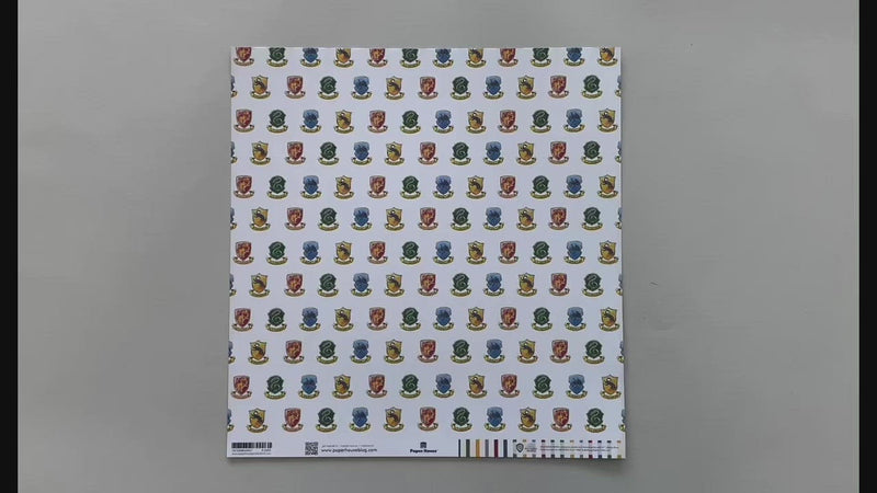 Female hands pick up harry potter scrapbook paper featuring a pattern of the multi-colored House Crests on one side and a pattern of colored stripes on the reverse.