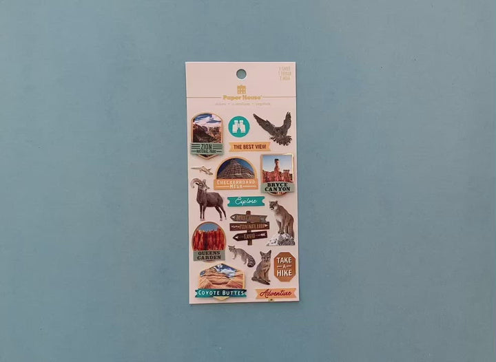 female hands display scrapbook stickers featuring animals and scenes from US national parks, and shows close up of one individual sticker.