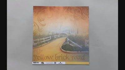 Female hands pick up scrapbook paper featuring the Yellow Brick Road on one side and a solid yellow on the other siide.