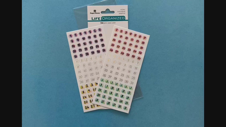 female hands displaying 2 sheets of planner stickers featuring numbers in colorful circles, on blue background with package.