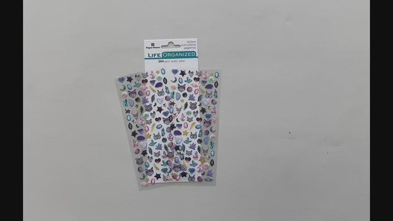 Female hands showing mini stickers featuring gold stars and gem-like foxes and owls, placing them down on surface with package and another sheet of mini stickers.