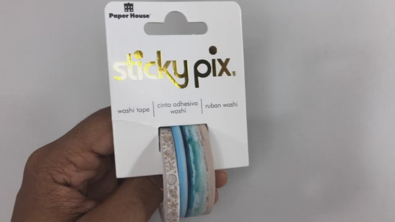 Hands pick up washi tape set in package featuring one roll of a photo real beach panorama and another roll of gold illustrated seashells.