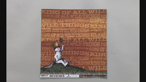 Female hands pick up scrapbook paper featuring Max from Where the Wild Things Are sitting on a hill on one side and a pattern of illustrated leaves on the other side.