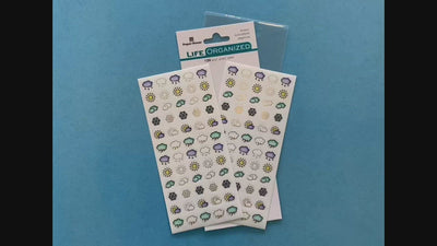 female hands displaying 2 sheets of planner stickers featuring illustrated clouds, suns and snowflakes, on blue background with package.