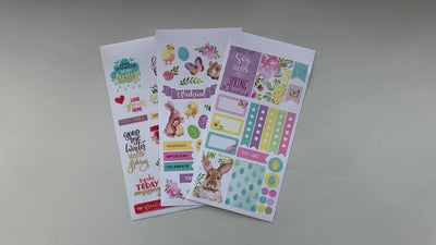 Female hands pick up and show in detail 3 sheets of stickers featuring Easter and April words and illustrations.