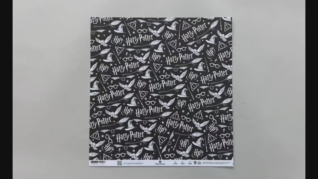 Female hands pick up harry potter scrapbook paper featuring white symbols and text on a black background on one side and a pattern of black glasses &amp; lightning bolts on a white background on the reverse.