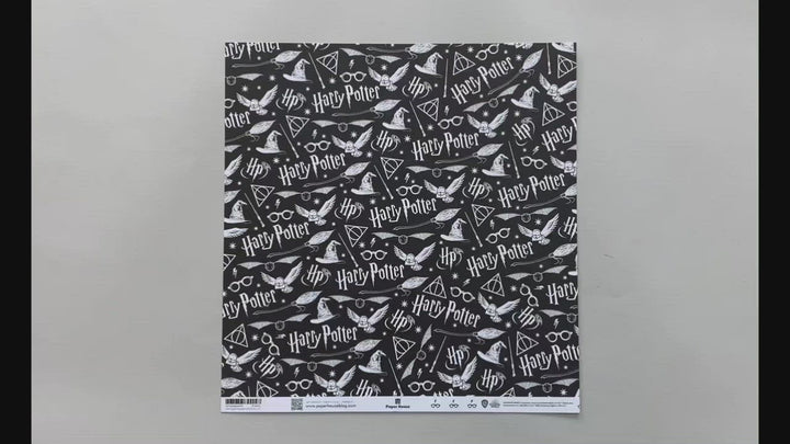 Female hands pick up harry potter scrapbook paper featuring white symbols and text on a black background on one side and a pattern of black glasses &amp; lightning bolts on a white background on the reverse.