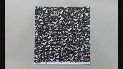 Female hands pick up harry potter scrapbook paper featuring white symbols and text on a black background on one side and a pattern of black glasses & lightning bolts on a white background on the reverse.