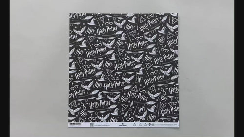 Female hands pick up harry potter scrapbook paper featuring white symbols and text on a black background on one side and a pattern of black glasses & lightning bolts on a white background on the reverse.