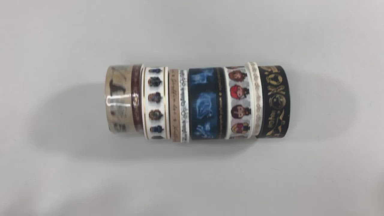 rolls of washi tape shown on white surface and being stretched out by hands to display the various Harry Potter images.